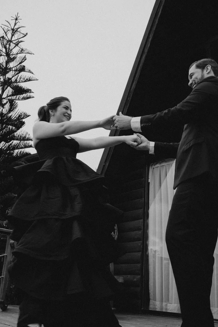Dan vueltas de la mano en el balcón de la cabaña, ella con el vestido negro