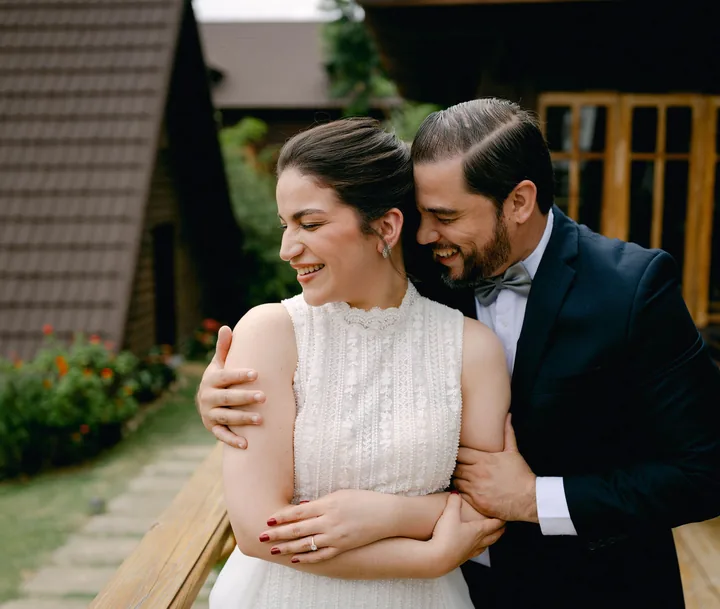 Él la abraza por detrás y ella, de blanco, ríe