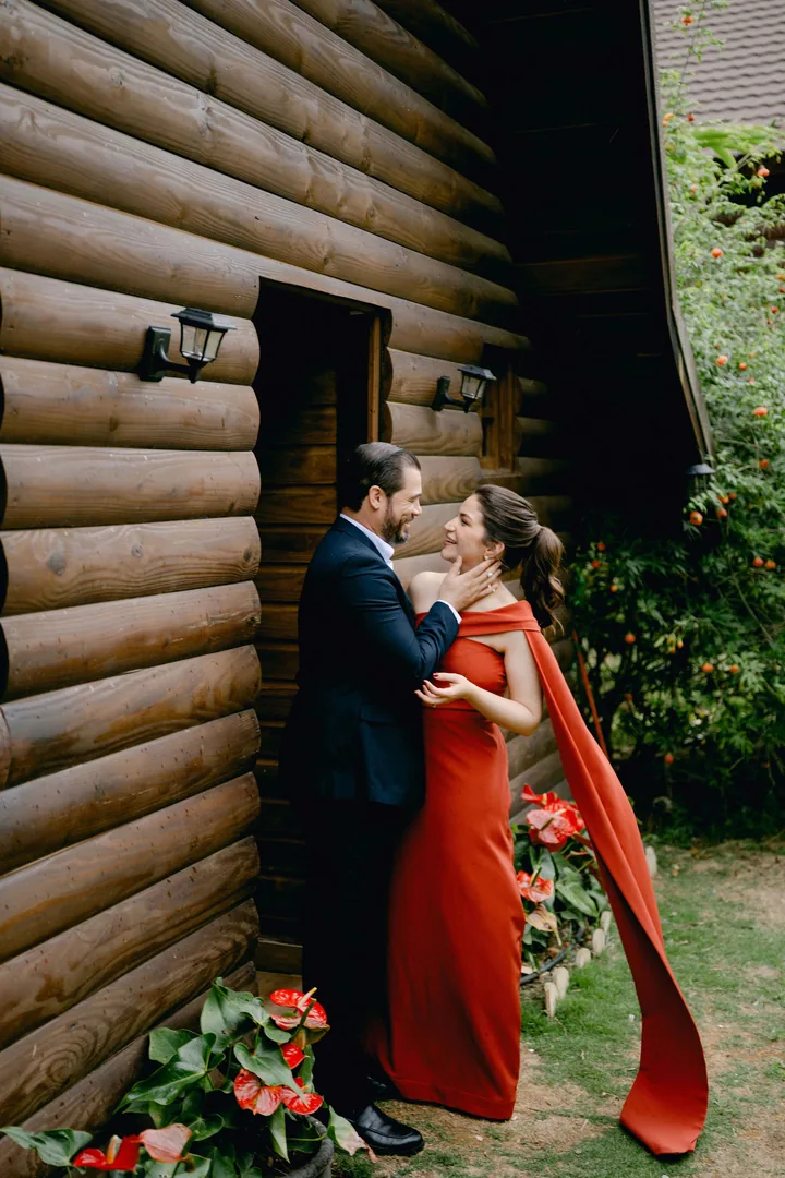 Junto a la puerta de la cabaña, ella con vestido rojo